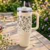 Beige tumbler with floral design on a wooden table with flowers and fruits in the background